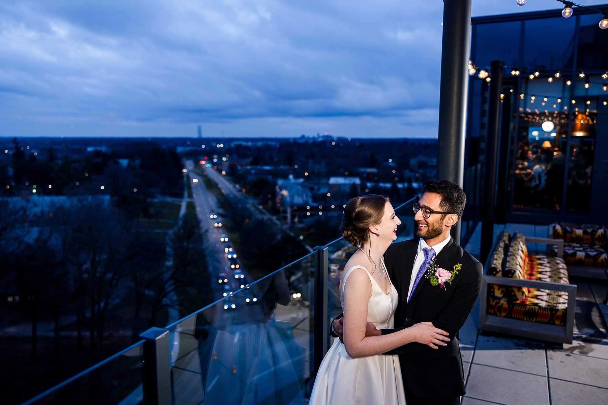 Wedding photographs of a bride and groom smiling while standing on the rooftop at the Graduate Hotel in East Lansing, Michigan at night with blue clouds