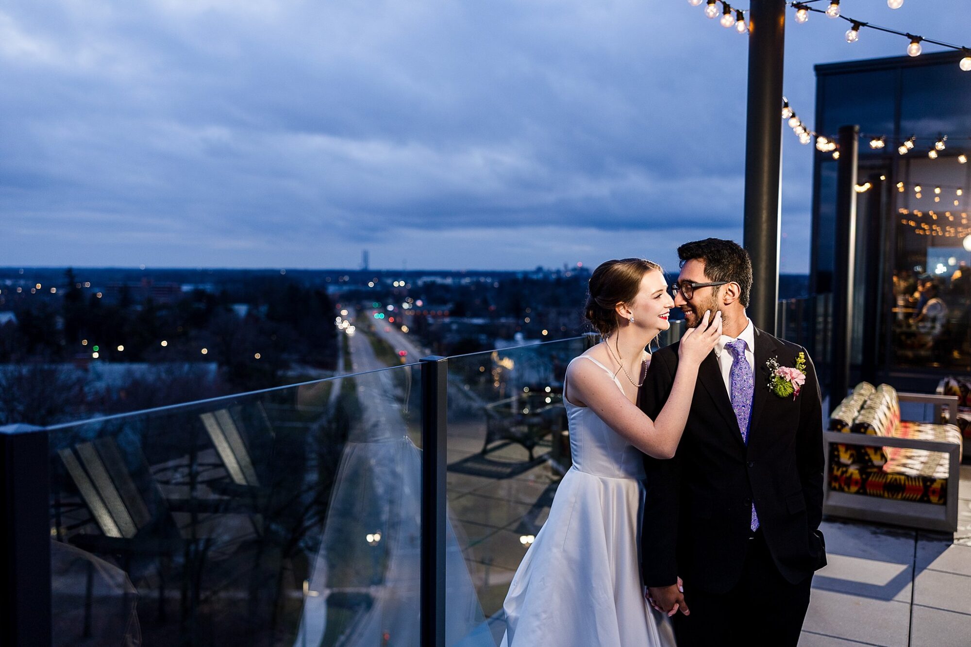 Wedding photographs of a bride and groom smiling while standing on the rooftop at the Graduate Hotel in East Lansing, Michigan at night with blue clouds